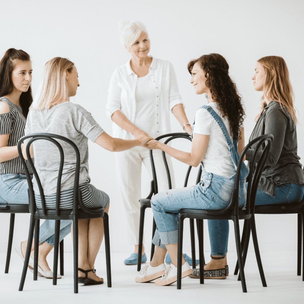 Women participating in a supportive group therapy session, holding hands and connecting in a safe and healing environment