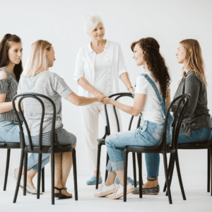 Women participating in a supportive group therapy session, holding hands and connecting in a safe and healing environment