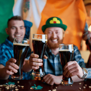 Friends toasting dark Irish beers at a St. Patrick’s Day celebration with Irish flag colors in the background