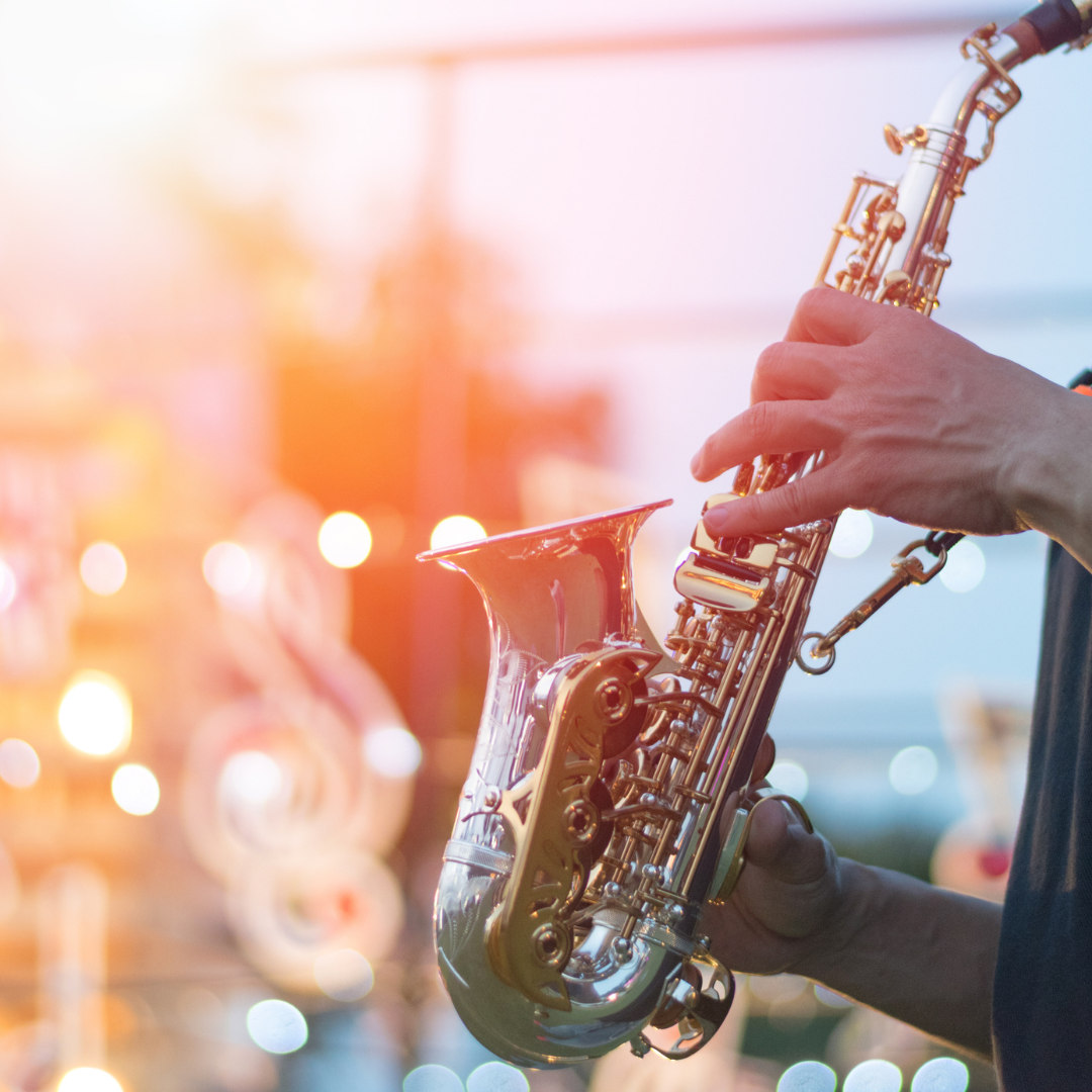 A musician plays a gleaming saxophone under warm stage lights with bokeh in the background — capturing the spirit of the 15th Annual Arlington Jazz Festival, April 8–12, 2026.