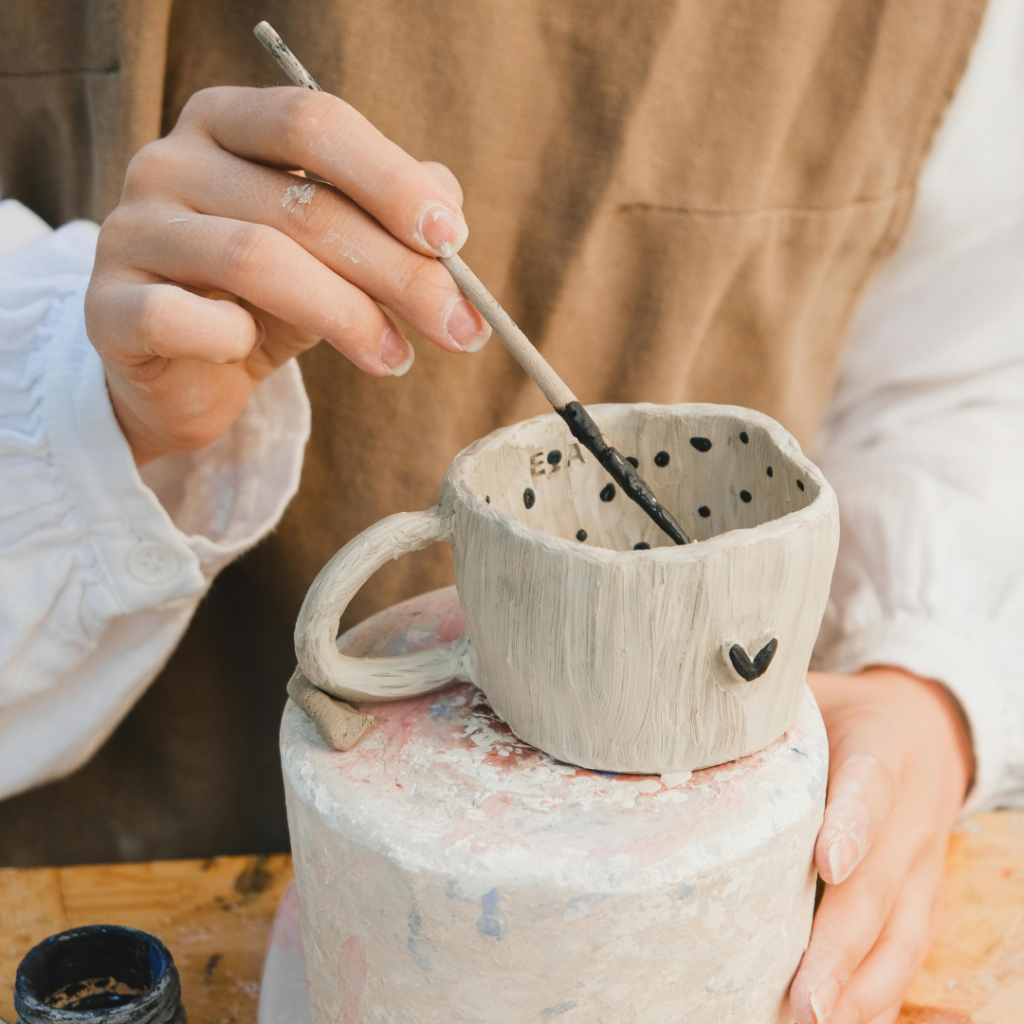 Person painting a handmade ceramic mug with black details at a pottery workshop, illustrating a local ceramics class event.